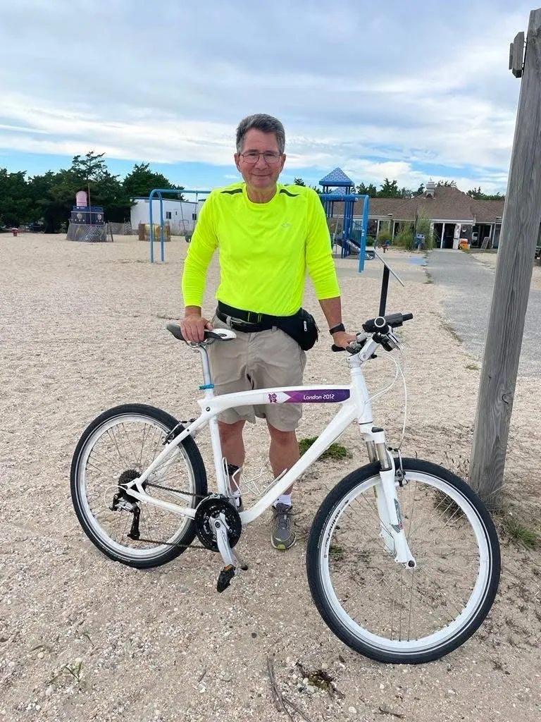A man in a high-visibility shirt with a measuring bicycle on a beach path.