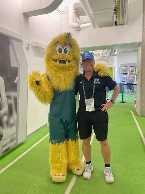 An official posing with the championships mascot on a green warm-up track.