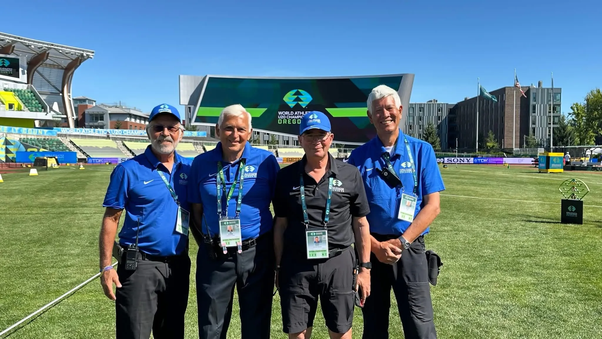 Four officials in blue shirts on a stadium infield.